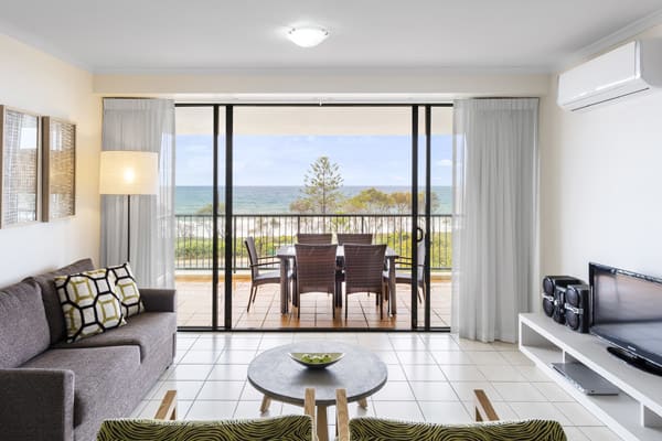 air conditioned 2 bedroom apartment living room with furniture and private balcony with tables and chairs and views of ocean at Oaks Seaforth Resort hotel, Sunshine Coast